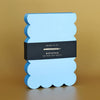 Blue scalloped notepad with a bright blue edge and black label on a brown background