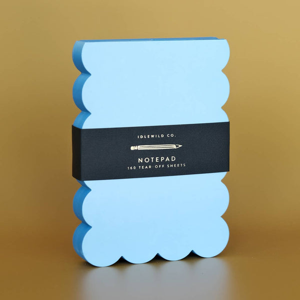 Blue scalloped notepad with a bright blue edge and black label on a brown background