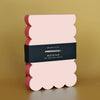 Pink and red scalloped notepad with a black label on a gold background