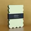 Light green notepad with scalloped olive green edges on a brown background