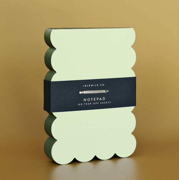 Light green notepad with scalloped olive green edges on a brown background