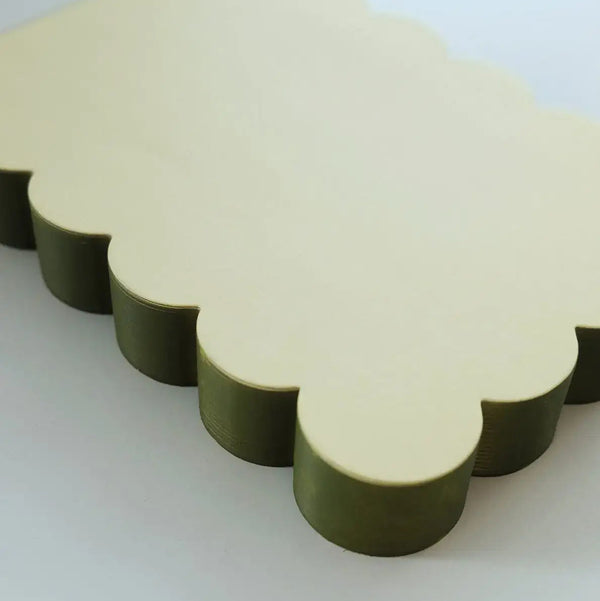 A close view of a scalloped notepad in light chartreuse green with dark olive edges against a light backdrop.