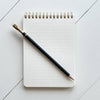 Lined notebook with a pencil on a light gray tiled surface.