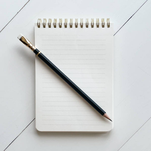 Lined notebook with a pencil on a light gray tiled surface.