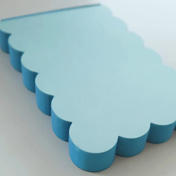 Detail of a light blue scalloped notepad with a bright blue edge on a white background.
