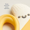 Silicone banan shaped teether with textured surface and smiling face design on a light background.