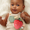 Baby holding a soft teether toy with a strawberry design on a white fluffy background