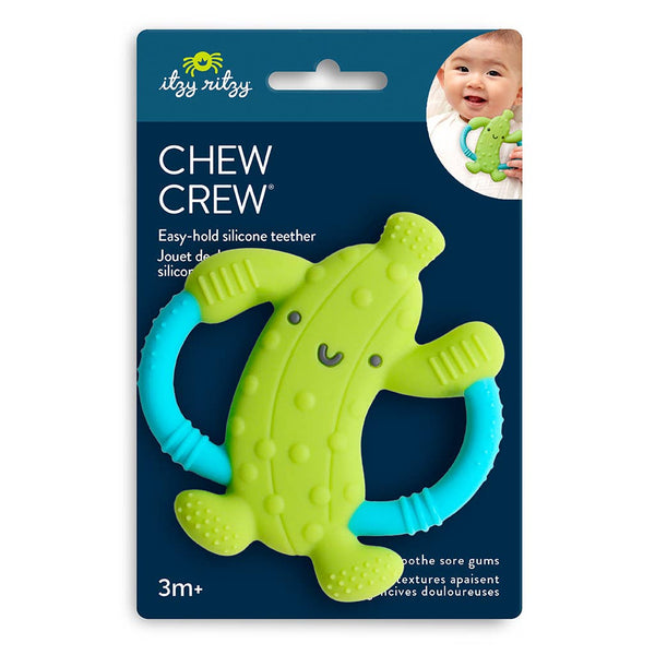 Green and blue pickle shaped silicone teether toy with grip handles on dark blue packaging against a white background.