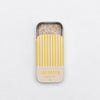 Small sliding tin container of lemon zest-infused sea salt with yellow striped lid on a white background