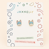 A pair of small French bulldog stud earrings displayed on a branded white backing card. The card shows the brand name JAXKELLY at the top, and the earrings feature pastel blue French bulldog faces with pink inner ears and cream/beige outlines.