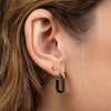 Close-up of an ear wearing gold hoop earrings and a champagne gemstone stud with a blurred background