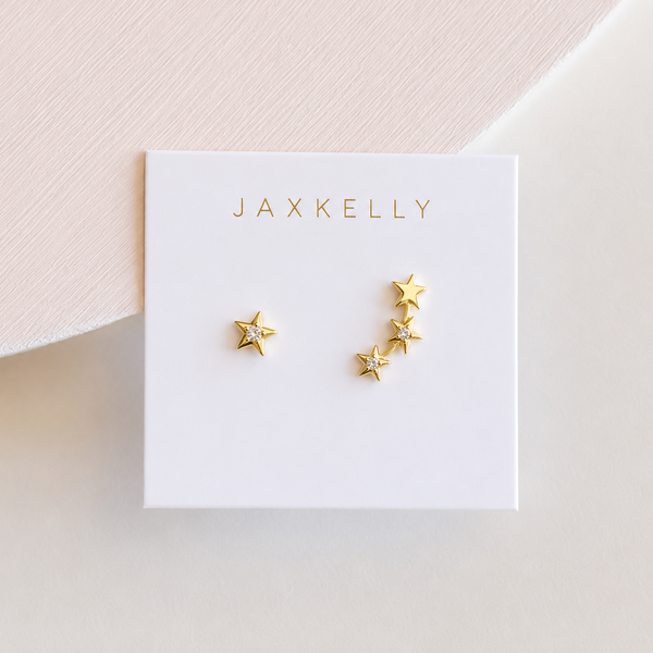 Gold star earrings with delicate white CZ stones on a Jaxkelly branded card against a light pink background