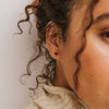 Close-up of a woman's ear with a black tourmaline stud earring against a neutral background