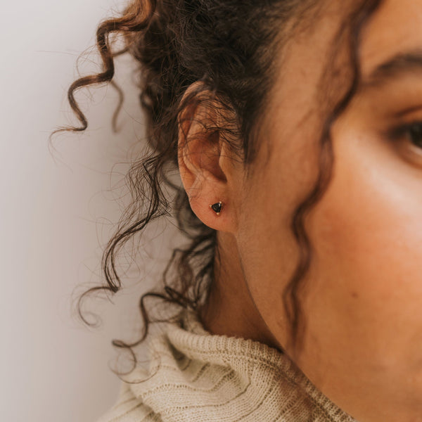 Close-up of a woman's ear with a black tourmaline stud earring against a neutral background