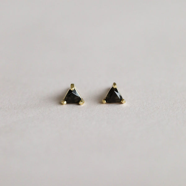 Pair of triangle-shaped black tourmaline gemstone earrings with gold settings on a light gray background