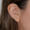 Close-up of an ear wearing a gold mushroom-shaped CZ pave stud earring with hair partially covering the frame.