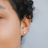 Close-up of an ear wearing a gold seashell earring with a blurred background