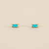 Pair of gold earrings with turquoise baguette stones on a beige background