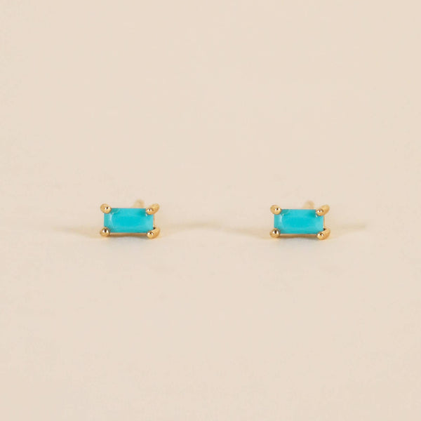 Pair of gold earrings with turquoise baguette stones on a beige background