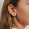A close up view of a person with light brown hair wearing a gold and white CZ stone double stud earring.