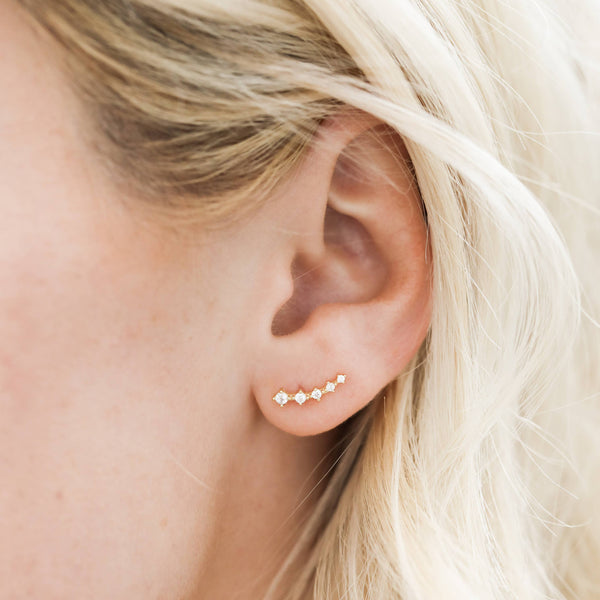 Close-up of an ear wearing a gold stud earring with small white CZ stones.
