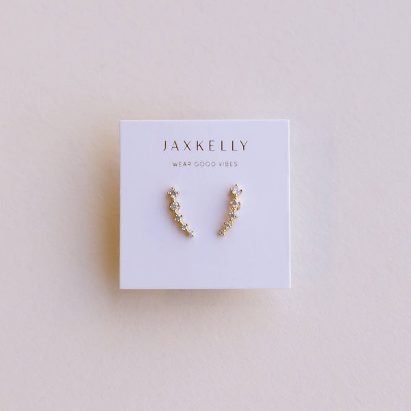 Pair of gold earrings with white CZ stones on a Jaxkelly branded card against a light background