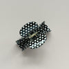 A black and white polka dot hair claw clip shown on a neutral light gray background.