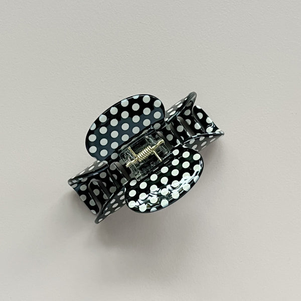 A black and white polka dot hair claw clip shown on a neutral light gray background.
