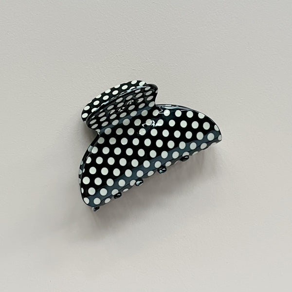 A glossy black hair claw clip with a white polka dot pattern, photographed against a neutral light gray background.