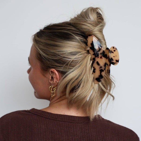 Person with blonde hair held up with a light tortoiseshell large claw clip against a white background