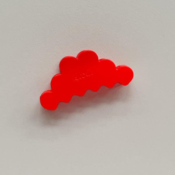 A bright red, cloud-shaped hair claw clip photographed on a neutral light gray background.
