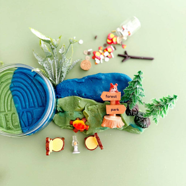 Toy play dough set with a blue mountain, trees, and small figures on a green background