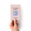 Hand holding a pink mini zine with text and a small illustration on a white background