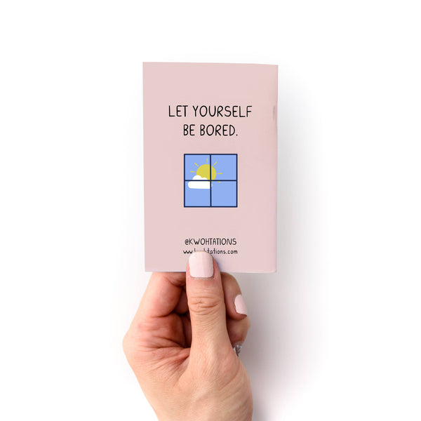 Hand holding a pink mini zine with text and a small illustration on a white background