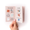 Hand holding a small zine with illustrated pages on activities like reading, writing, and socializing.