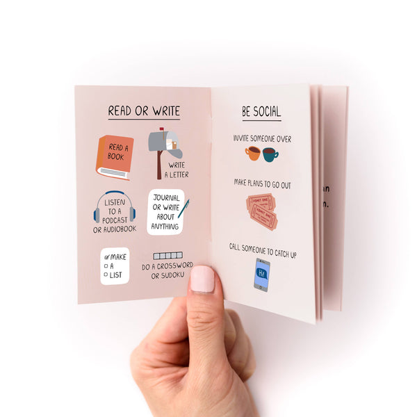 Hand holding a small zine with illustrated pages on activities like reading, writing, and socializing.