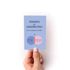 Hand holding a mini zine titled 'Reminders for Uncertain Times: from one human to another" and venn diagram design on a white background