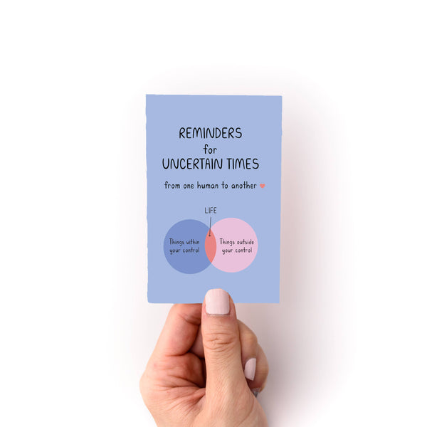 Hand holding a mini zine titled 'Reminders for Uncertain Times: from one human to another" and venn diagram design on a white background