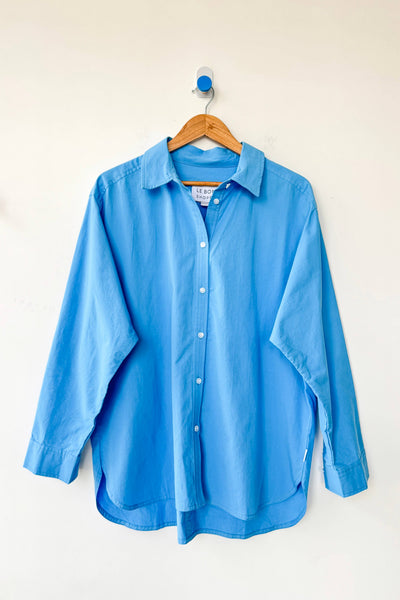 Blue shirt on a wooden hanger against a white wall