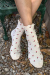 White socks with red floral patterns worn by a person sitting on a green bench.
