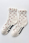 White ruffled socks with dainty red and green flowers and black grippy soles on a light gray background