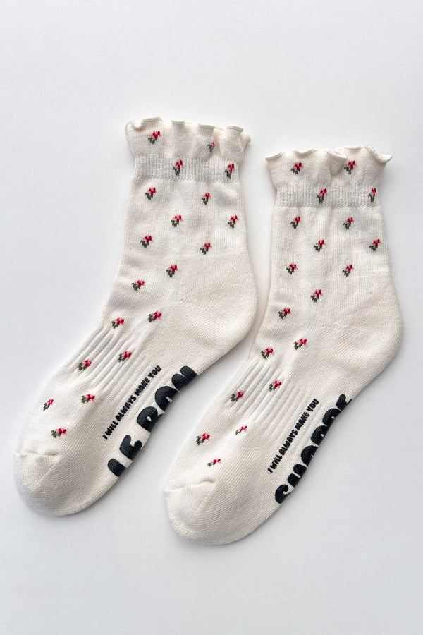 White ruffled socks with dainty red and green flowers and black grippy soles on a light gray background