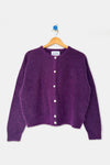 A rich purple mohair cardigan with white buttons hanging on a wood hanger against a white wall.