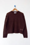 A rich brown mohair blend crewneck sweater hanging on a wood hanger against a white wall.