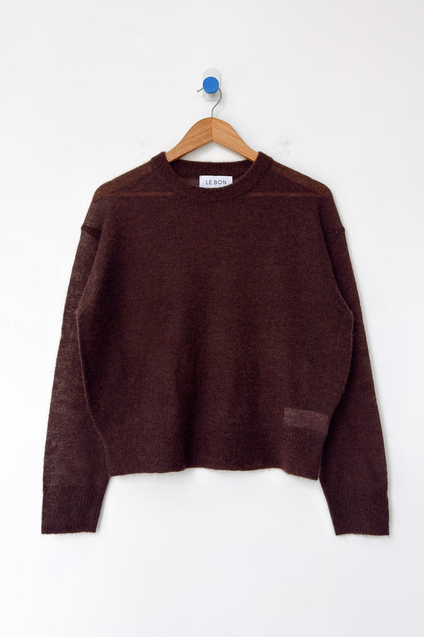 A rich brown mohair blend crewneck sweater hanging on a wood hanger against a white wall.