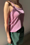 Person wearing a pink tank top and green pants against a plain background