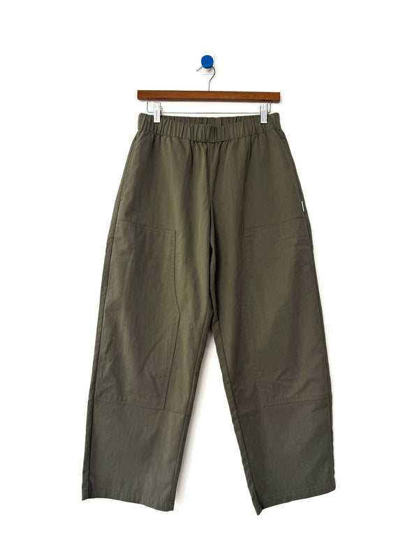 A pair of army green cotton-nylon elastic waist pants on a wood hanger against a white wall. 