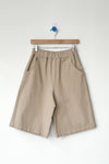 Beige bermuda shorts hanging on a wooden hanger against a white background
