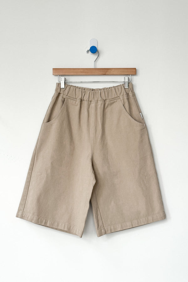 Beige bermuda shorts hanging on a wooden hanger against a white background
