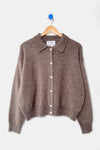 A brown knit cardigan sweater with a pointed collar and white buttons, hanging on a wooden hanger against a light gray background.